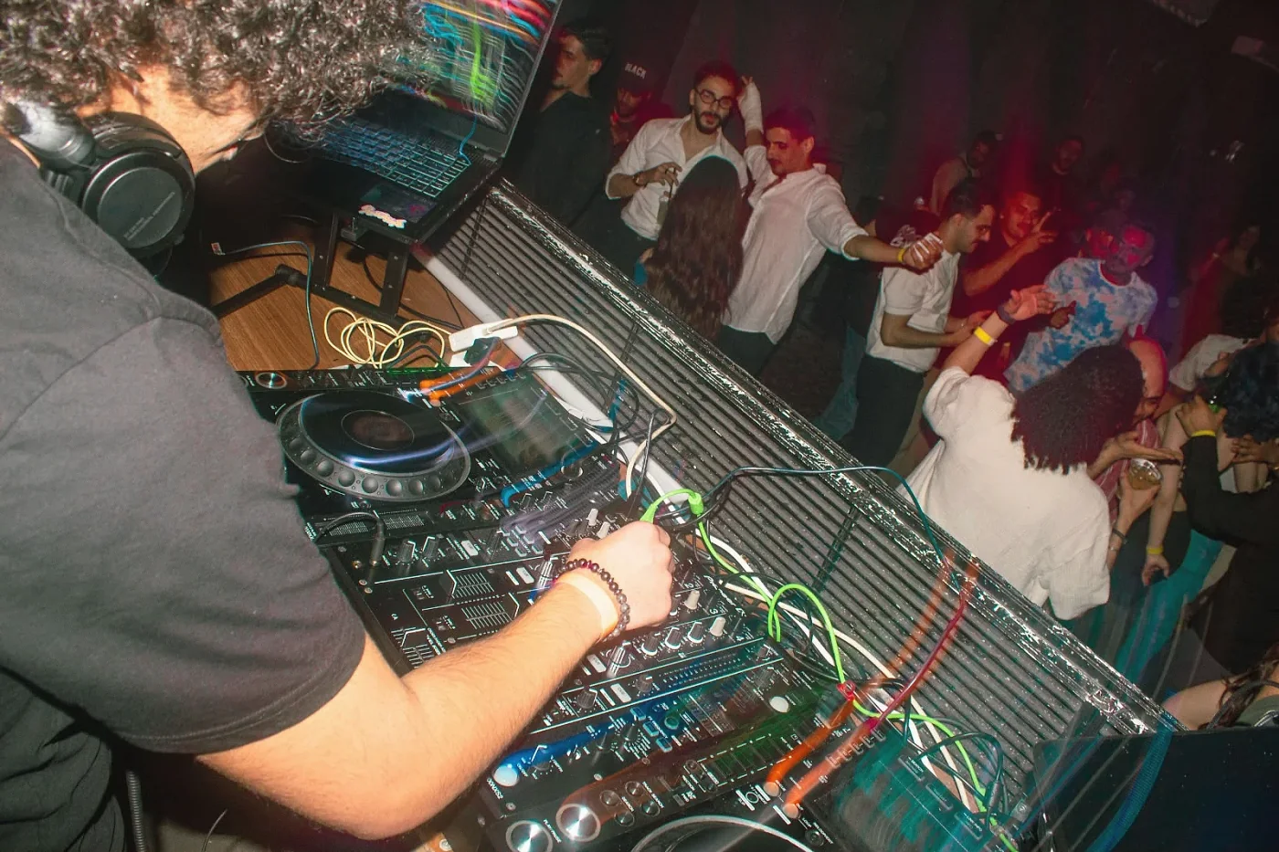 Anas at the mixer, seen from behind, with the crowd dancing on the other side of the booth